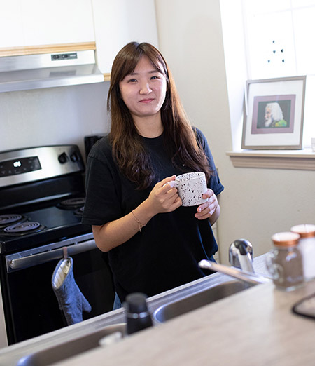Female student drinking a cup of coffee in the kitchen of a student housing living space. Photo courtesy of South Puget Sound Community College