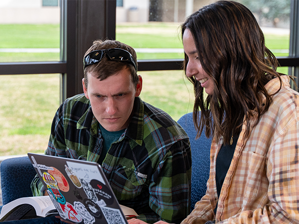 Two sitting students looking at a laptop screen