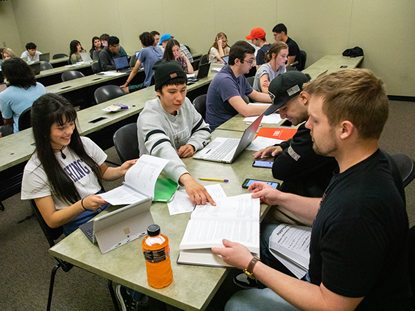 Students in classroom talking over books and papers